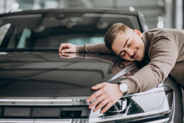 Young handsome man hugging a car in a car showroom