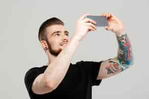 Free photo young handsome man looking at phone over grey wall.