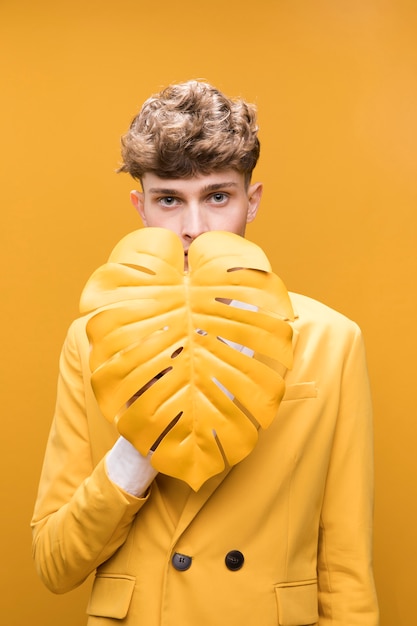 Young handsome man behind palm leaf in a yellow scene