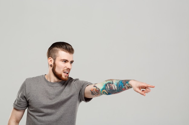 Free photo young handsome man pointing finger in side over grey wall.