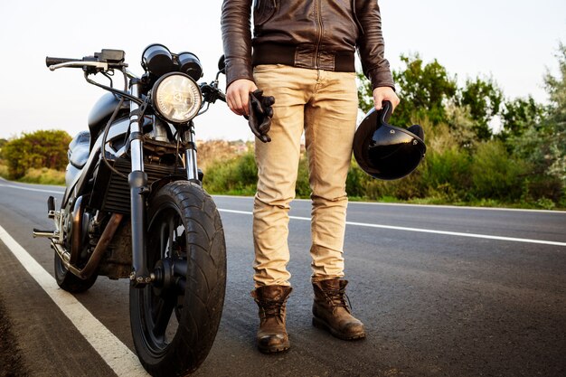 Young handsome man posing near his motorbike at countryside road.