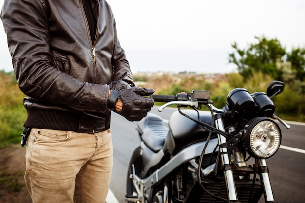 Young handsome man posing near his motorbike, wearing gloves.