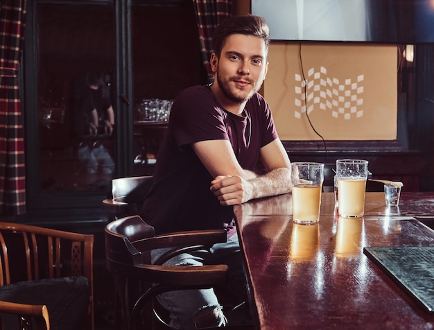 Free photo young handsome man resting in the bar or pub, sitting with a glass of beer at wooden counter.