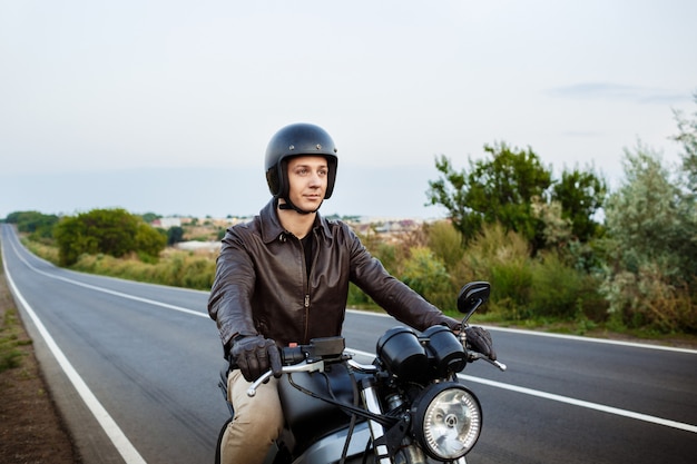 Young handsome man riding on motorbike at countryside road.