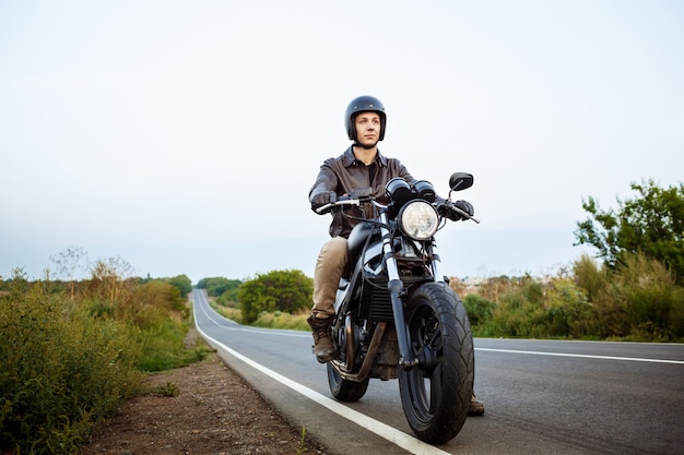 Young handsome man riding on motorbike at countryside road.