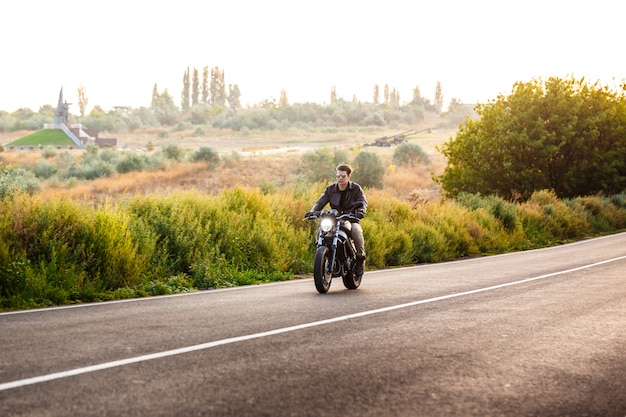 Young handsome man riding on motorbike at countryside road.