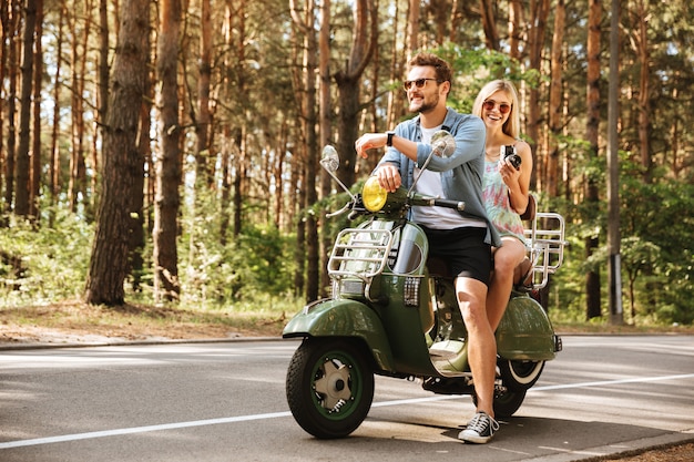 Free photo young handsome man on scooter with womanfriend holding camera