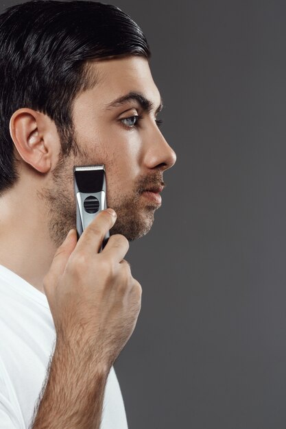 Young handsome man shaving over grey wall