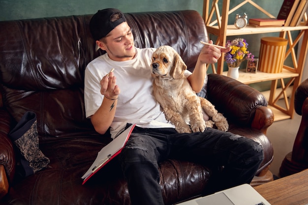 Young handsome man sitting on brown sofa and working with his cute dog