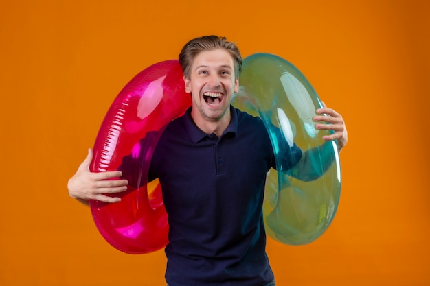 Free Photo young handsome man standing with inflatable rings surprised and happy with wide open mouth over orange background