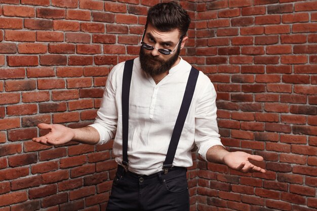 Young handsome man in sunglasses gesturing posing on brick wall.