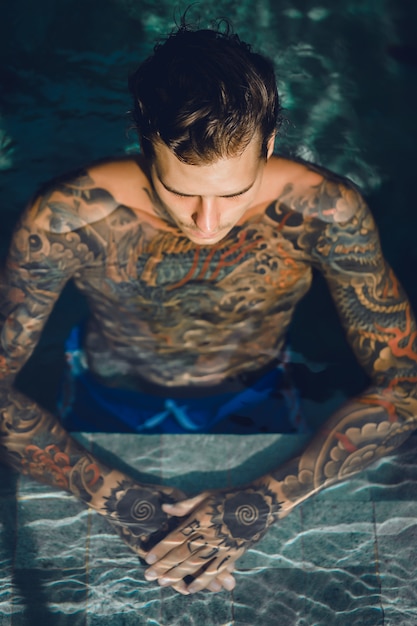 young handsome man in tattoos resting in the outdoor pool. 