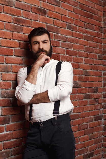 Young handsome man thinking posing on brick wall.