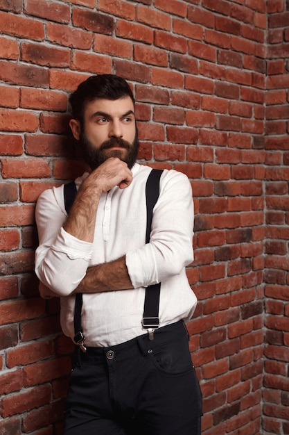 Young handsome man thinking posing on brick wall.