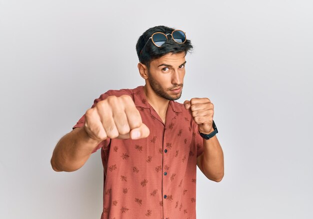 Young handsome man wearing casual summer clothes punching fist to fight aggressive and angry attack threat and violence