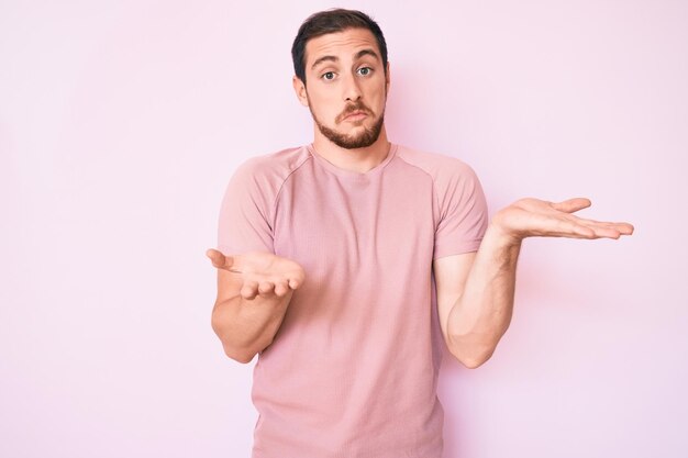 Young handsome man wearing casual tshirt clueless and confused expression with arms and hands raised doubt concept