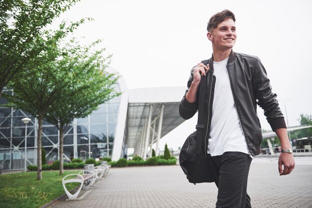 Young handsome man with a bag on his shoulder in a hurry to the airport.