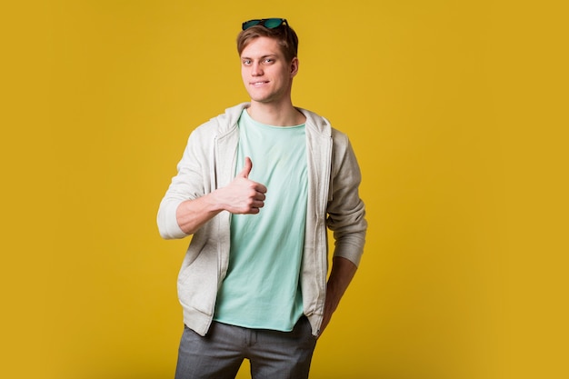 Free photo young handsome man with beard standing over yellow wall smiling with happy face looking and pointing to the side with thumb up.