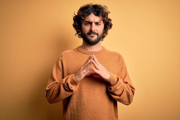 Free photo young handsome man with beard wearing casual sweater standing over yellow background hands together and fingers crossed smiling relaxed and cheerful success and optimistic