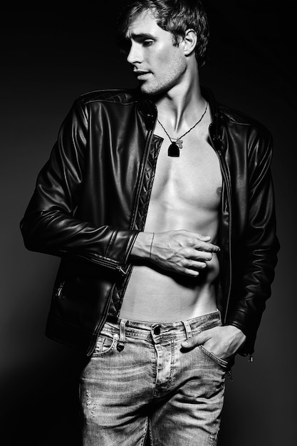 Free photo young handsome muscled fit male model man posing in studio showing his abdominal muscles in  leather jacket