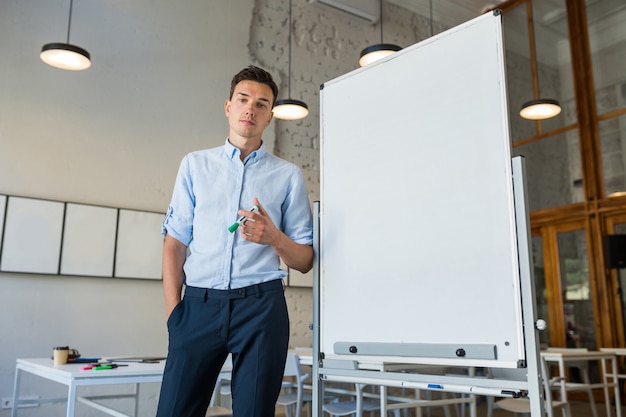 Free photo young handsome smiling man standing at empty white board with marker