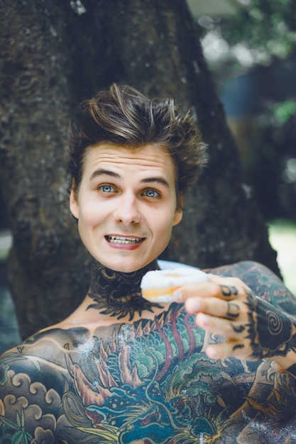 young handsome tattooed man having breakfast in bed in the open air outdoors in the garden