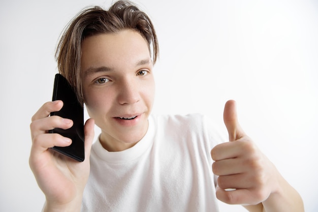 Young handsome teenager showing smartphone screen and signing OK sign isolated on gray background. Human emotions, facial expression, advertising concept.