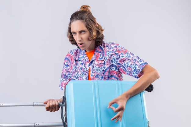 Young handsome traveler guy holding suitcase using as a guitar looking with serious confident expression on face standing 