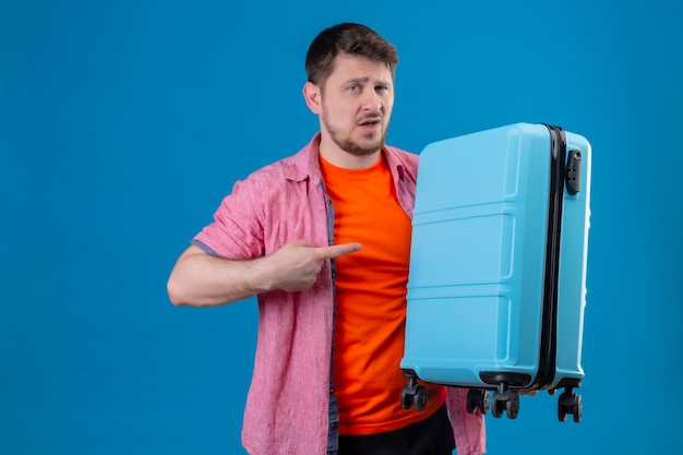 Free Photo young handsome traveler man holding suitcase with suspicious expression