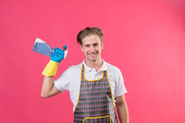 Young hansdome man wearing apron and rubber gloves holding cleaning spray