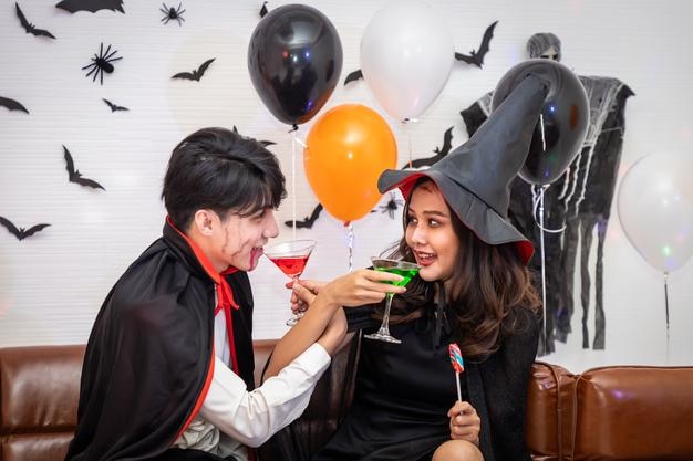 Young happy Asian couple dressing Halloween costume vampire and witch celebrating in party Holding and clinking wine glass Looking at camera