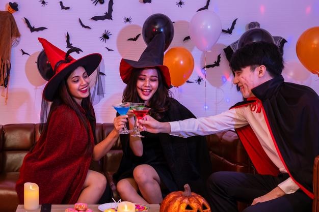 Free photo young happy asian people dressing halloween costume vampire and witch celebrating in party holding and clinking wine glass