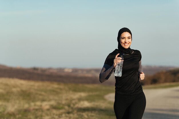 Young happy athletic woman carrying bottle of water while running in nature Copy space