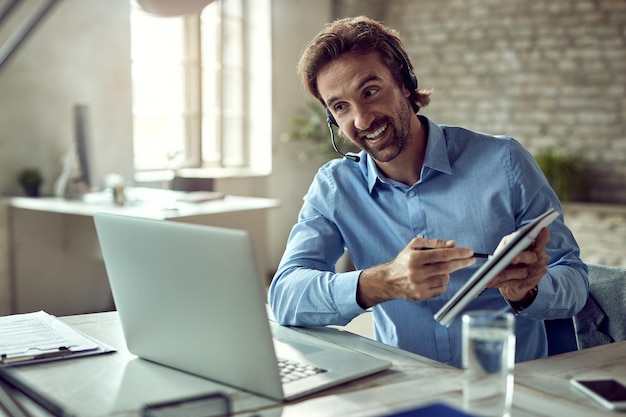 Free Photo young happy businessman using laptop while having online meeting from his office