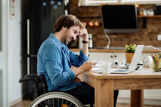 Free photo young happy businessman in wheelchair working at home and text messaging on mobile phone.