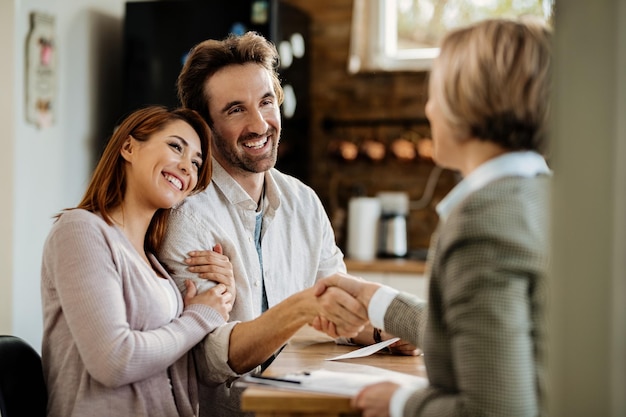 Young happy couple came to an agreement with their insurance agent. Focus is on man shaking hands with the agent.