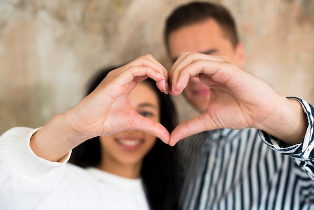 Young happy couple gesturing heart with hands