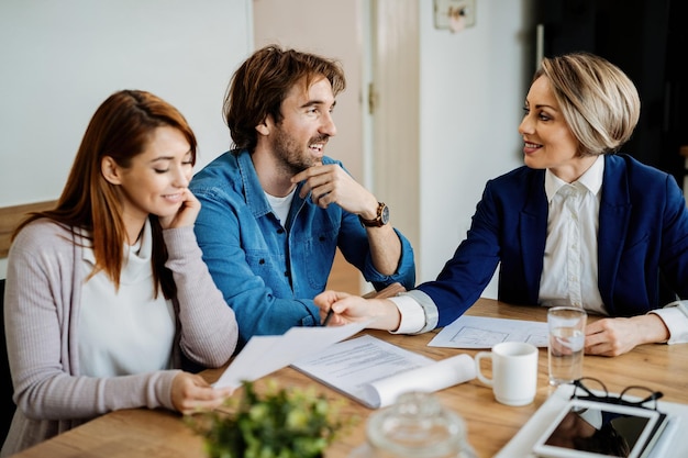 Young happy couple and insurance agent talking while analyzing paperwork during consultations.