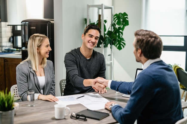 Young happy couple making an agreement with their financial advisor at home Men are shaking hands