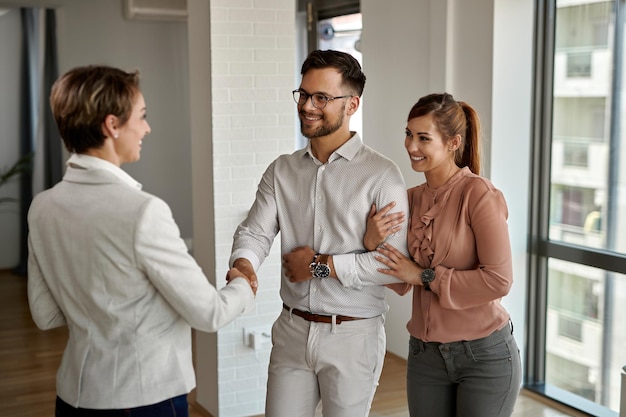 Young happy couple shaking hands with real estate agent while buying a new apartment