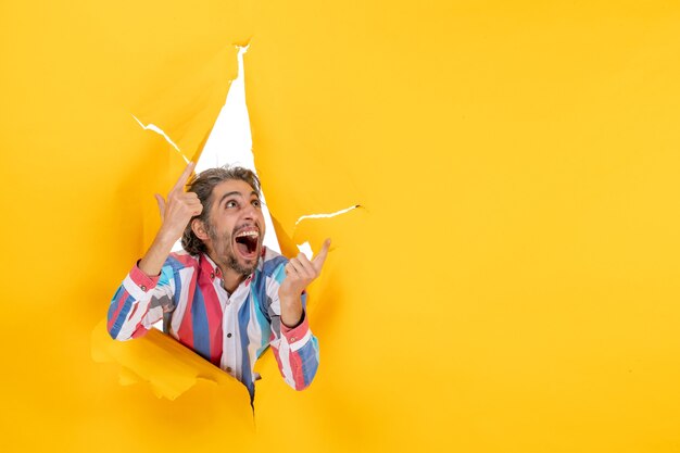 Young happy emotional bearded guy in a torn hole and free space in yellow paper