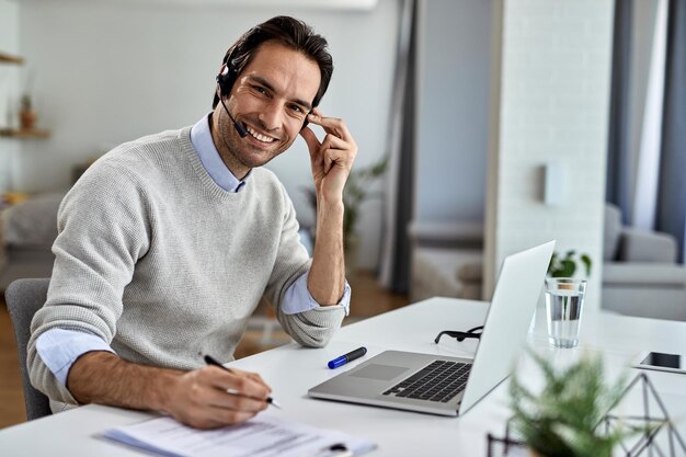 Young happy entrepreneur using laptop and writing reports while working at home