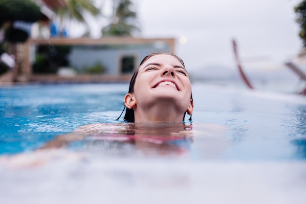 Young happy fit slim european woman in bright pink bikini blue swimming pool