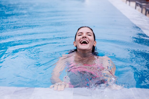 Young happy fit slim european woman in bright pink bikini blue swimming pool