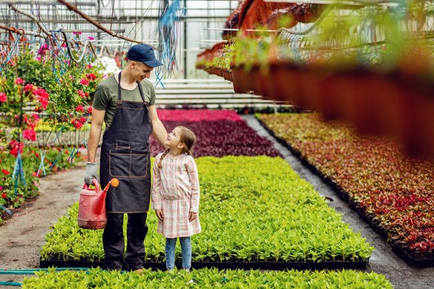 Young happy florist with watering can talking to a little girl at plant nursery