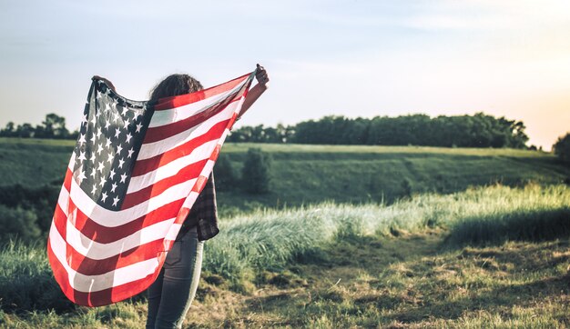 Young happy girl running and jumping carefree with open arms over wheat field. Holding USA flag.