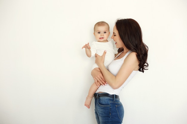 Young happy mother smiling holding looking at her baby daughter over white wall.