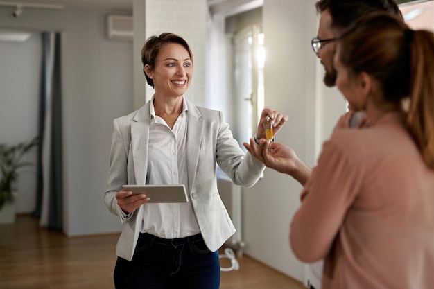 Young happy real estate agent giving house keys to a couple who is buying a new home