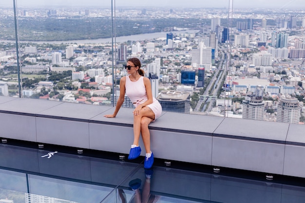 Free Photo young happy smiling caucasian woman traveller in fitting dress and sunglasses on high floor in bangkok