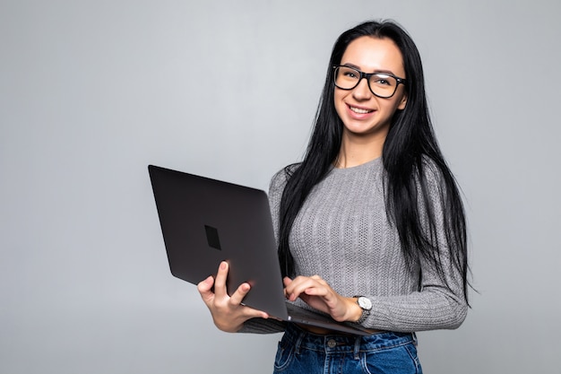 Young happy smiling woman in casual clothes holding laptop isolated on gray wall